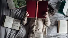 Una bambina legge sdraiata su un letto pieno di libri