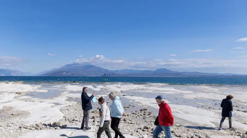 Alcune persone camminano e scattano foto sulle rocce emerse dal promontorio di Sirmione - Foto New Reporter Nicoli © www.giornaledibrescia.it
