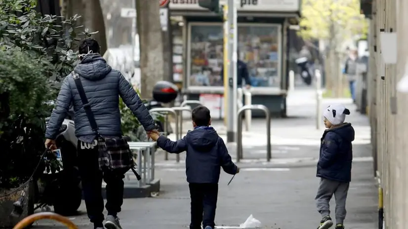 Un padre con i suoi figli passeggiano per strada - Foto Ansa  © www.giornaledibrescia.it
