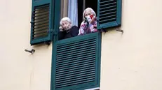 Due donne anziane chiuse in casa si affacciano alla finestra: una indossa una mascherina tricolore - Foto Ansa © www.giornaledibrescia.it