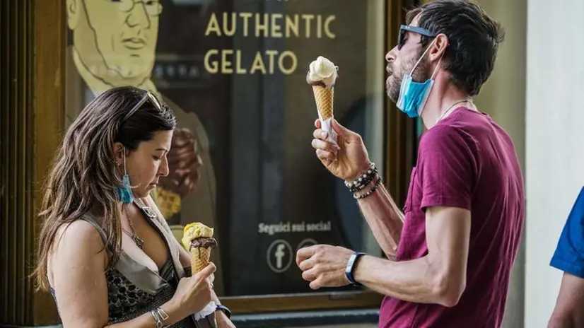Due ragazzi abbassano la mascherina per mangiare un gelato all'aperto - Foto Ansa/Tino Romano