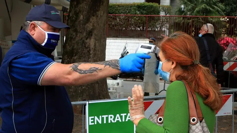 Un addetto alla sicurezza prova la febbre con un termometro a pistola fuori da un mercato all'aperto - Foto Ansa/Paolo Salmoirago