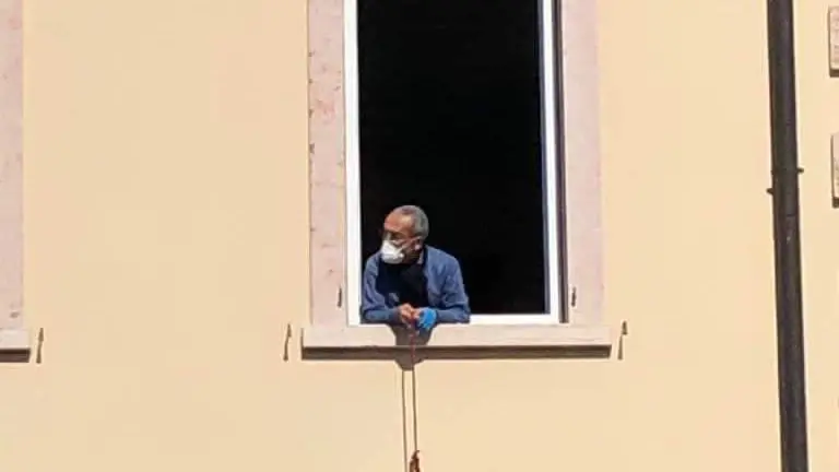 Il sindaco Caimi affacciato alla finestra del municipio, sede, durante l'emergenza, del gruppo di volontariato «CoronaVita», per la produzione di mascherine artigianali - Foto © www.giornaledibrescia.it