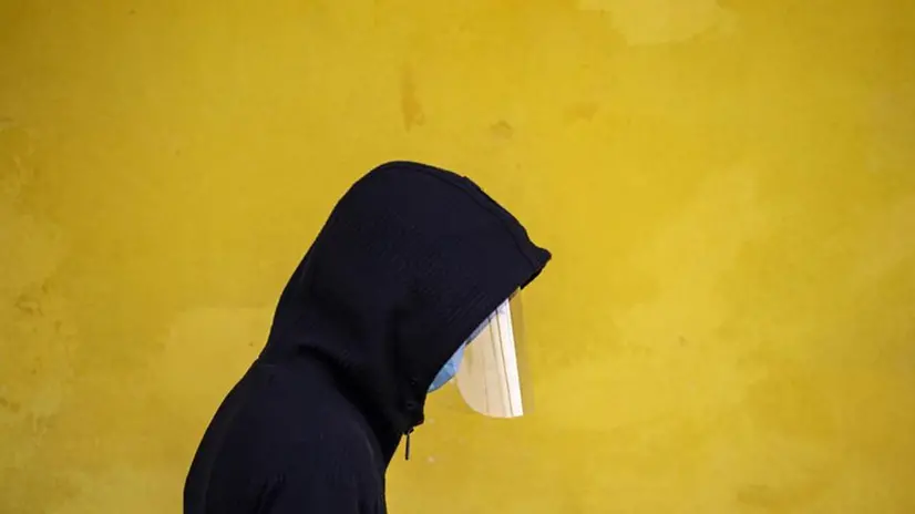 Una persona indossa una mascherina e una visiera anti Covid - Foto Ansa  © www.giornaledibrescia.it