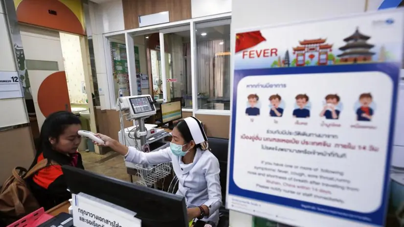 Un'infermiera controlla una paziente in Thailandia: in primo piano un cartello informativo sul Coronavirus - Foto Ansa/Epa Rungroj Yongrit © www.giornaledibrescia.it