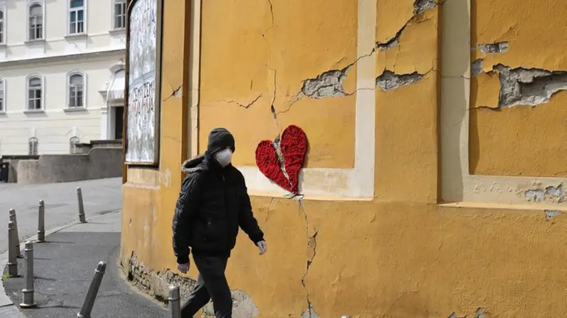Un uomo col volto coperto da una mascherina passa accanto al murales Broken Heart, realizzato a Zagabria dall'artista Ivona
