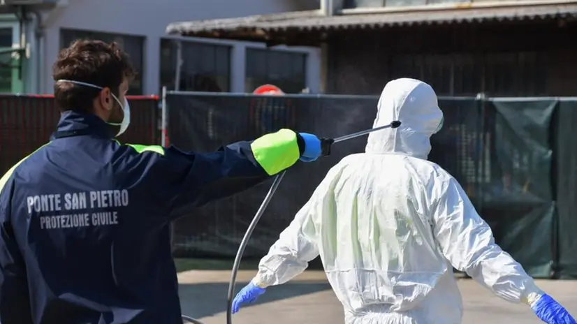 La disinfezione della tuta indossata da una persona impegnata nelle operazioni contro il coronavirus - Foto Ansa © www.giornaledibrescia.it