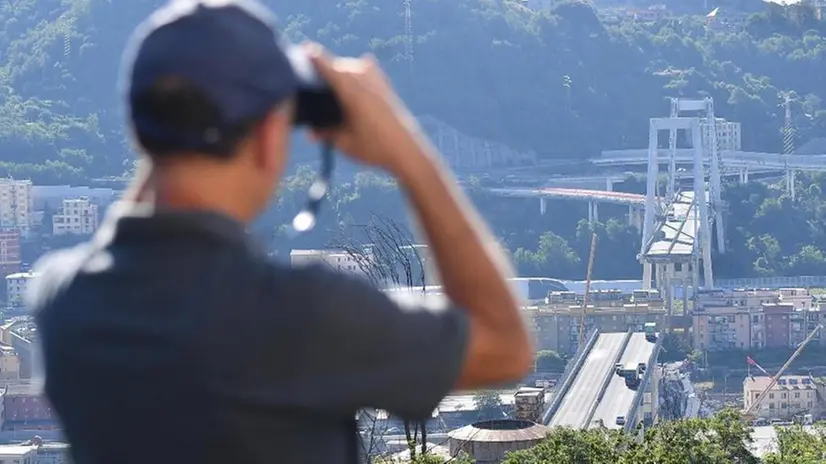 Un uomo osserva con il binocolo il disastro del ponte Morandi - Foto Ansa