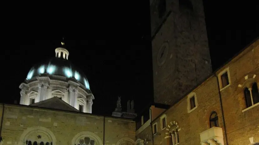 Di sera. Una guida illustra il Palazzo del Broletto ad alcuni turisti