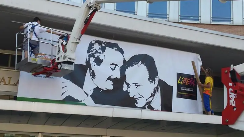 La foto di Falcone e Borsellino mentre viene issata al Palagiustizia - © www.giornaledibrescia.it