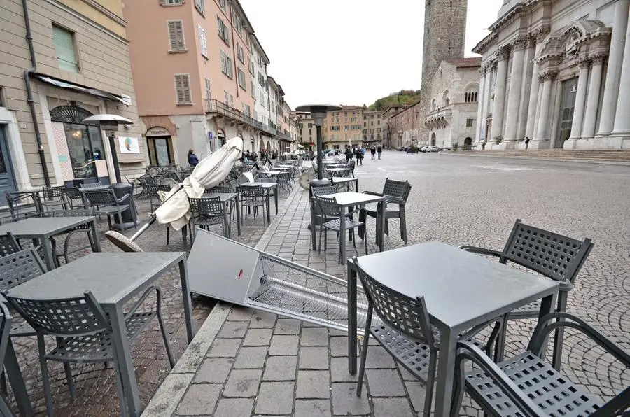Tavolini, ombrelloni e "funghi" ribaltati dallo stravento all'esterno dei locali di piazza Paolo VI, in centro a Brescia
