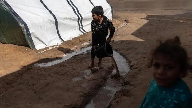 epa11107815 An internally displaced Palestinian child (L) pours water following a rainy night at Rafah Camp, southern Gaza Strip, 27 January 2024. Since 07 October 2023, up to 1.9 million people, or more than 85 percent of the population, have been displaced throughout the Gaza Strip, some more than once, according to the United Nations Relief and Works Agency for Palestine Refugees in the Near East (UNRWA), which added that most civilians in Gaza are in 'desperate need of humanitarian assistance and protection'.  EPA/HAITHAM IMAD