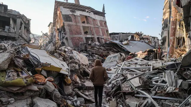 epa10460176 A man walks next to collapsed buildings after a powerful earthquake in Hatay, Turkey, 11 February 2023. More than 24,000 people have died and thousands more are injured after two major earthquakes struck southern Turkey and northern Syria on 06 February. Authorities fear the death toll will keep climbing as rescuers look for survivors across the region.  EPA/ERDEM SAHIN