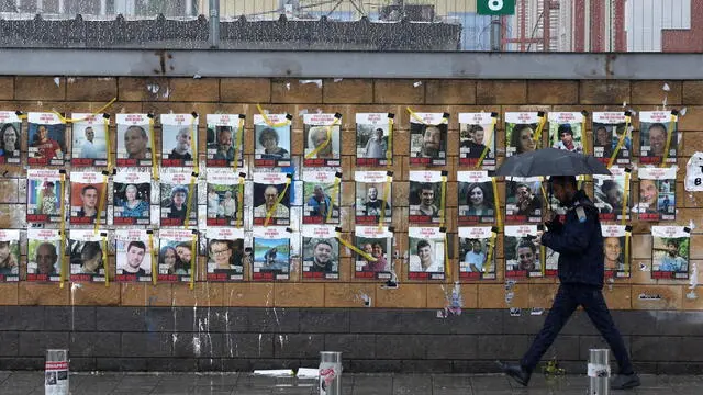 epa11125713 A man holding an umbrella walks past a display of pictures of Israeli hostages held by Hamas in Gaza, outside the Kirya military headquarters in Tel Aviv, Israel, 04 February 2024. According to the Israeli military, 136 Israelis, who were abducted and taken to the Gaza Strip during the 07 October 2023 attacks by Hamas, remain in captivity. Rallies in Israel have been critical of the government as they demand an immediate release of all the hostages.  EPA/ABIR SULTAN
