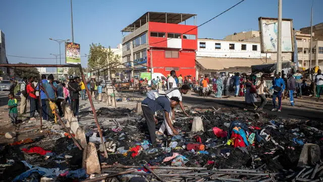 epa11141616 Two men walk through the charred remains of market stalls torched during protests the previous day in Dakar, Senegal, 10 February 2024. Violent clashes between opposition activists and security forces erupted after a recent law passed by the National Assembly postponed the presidential election to 15 December 2024 and also extended President Macky Sall's term of office by 10 months. The presidential election was originally scheduled to take place on 25 February 2024.  EPA/JEROME FAVRE