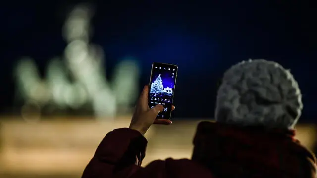 epa08851552 A woman takes a photo with a smartphone of a Christmas tree in front of the Brandenburg Gate in Berlin, Germany, 29 November 2020. Christmas markets and Christmas trees on public spaces are part of the traditional advent season in Germany. Due to the Coronavirus pandemic, Christmas markets have been canceled in Berlin the year 2020. EPA/CLEMENS BILAN