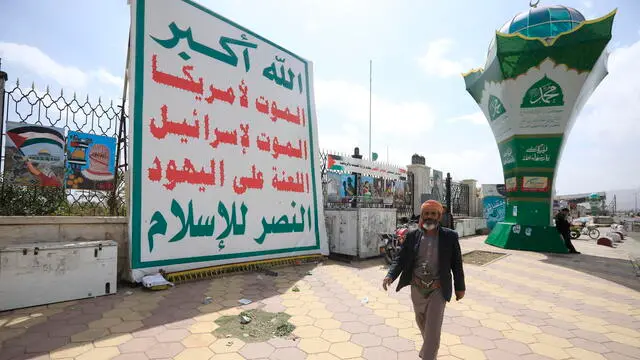 epa11147575 A person passes a banner depicting the official slogan of the Houthi movement which read 'Allah is the greatest of all, death to America, death to Israel, a curse on the Jews, victory to Islam', on the death anniversary of founder of the Houthi movement, Hussein al-Houthi, in Sana’a, Yemen, 12 February 2024.. The slain founder of the Houthi movement, Hussein al-Houthi, had coined the official slogan of the Shiite movement in 2002 before being killed in the 2004 conflict between his fighters and the former regime of Yemen. Following his brother's death, Abdul-Malik al-Houthi took over as leader of the Houthis 20 years ago, seizing control the capital Sana'a‚ and much of north Yemen in 2014. EPA/YAHYA ARHAB