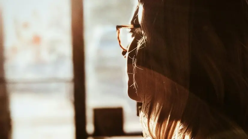 Una ragazza guarda fuori dalla finestra in un momento di riflessione - Foto Unsplash