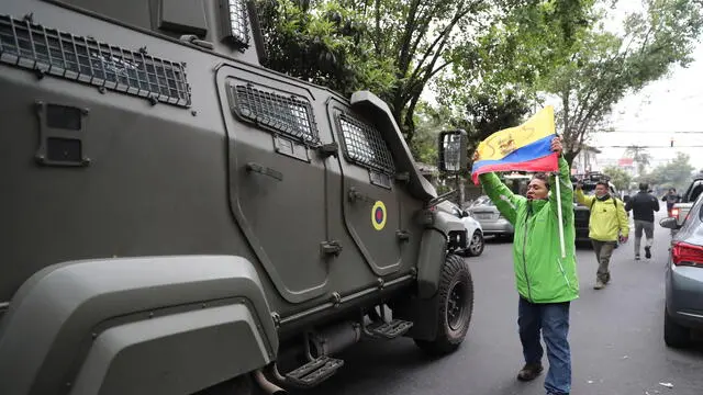 epa11262491 A man exhibits a national flag in front of an armored vehicle allegedly transporting former Ecuadorian Vice President Jorge Glas to the airport in Quito, Ecuador, 06 April 2024. Glas, Vice President during Rafael Correa and Lenin Moreno's presidential terms (2007-2017), convicted of corruption, was detained in the Mexican embassy facilities in Quito on 05 April 2024. Mexico broke diplomatic ties with Ecuador for the operation in the embassy to detain Glas, who was moved to the La Roca jail early 06 April 2024. EPA/Jose Jacome