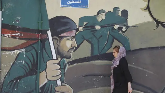 epa11277896 An Iranian woman walks next to a wall painting of Iranian revolutionary gaurd corps (IRGC) soldiers in Tehran, Iran, 14 April 2024. Iran's Islamic Revolutionary Guards Corps (IRGC) launched drones and rockets towards Israel late on 13 April 2024, Iranian officials said. EPA/ABEDIN TAHERKENAREH