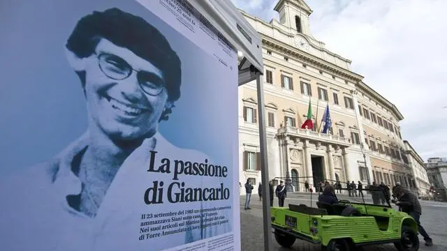 La Mehari del film Fortàpasc, l'auto scoperta del giornalista del Mattino Giancarlo Siani, assassinato dalla camorra, E l'immagine di Siani esosto su un grande poster. davanti alla Camera dei Deputati. 26 novembre 2013 a Roma. Per commemorare Siani l'automobile inizia un viaggio attraverso i luoghi della sua quotidianità - le strade, la scuola e sino al suo giornale - guidata da giornalisti, amici e persone impegnati nella lotta alla mafia. ANSA/MASSIMO PERCOSSI
