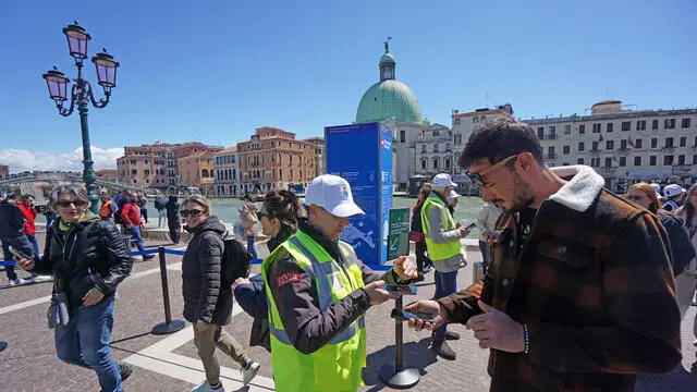 Un’operatrice ai varchi controlla il ticket di accesso sul telefonino di un turista, al check point del piazzale della stazione ferroviaria, Venezia 25 aprile 2024. ANSA/ANDREA MEROLA