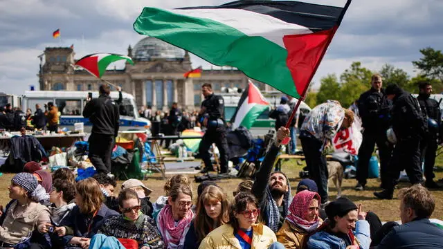 epa11302587 A protester sitting on the ground waves a Palestinian flag as police officers try to dismantle a pro-Palestine protest camp, in front of the Reichstag building in Berlin, Germany, 26 April 2024. A pro-Palestine protest camp set up at the Berlin Chancellery was closed and deconstructed by Berlin Police after repeated criminal offenses and violations of the restrictions, Berlin Police said. EPA/CLEMENS BILAN