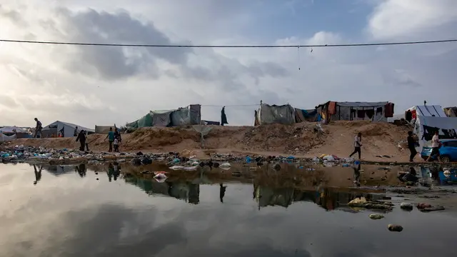 epa11303567 Palestinians walk next to a sewage spill near tents for internally displaced people at a temporary camp in Rafah camp, southern Gaza Strip, 26 April 2024. Since 07 October 2023, up to 1.7 million people, or more than 75 percent of the population, have been displaced throughout the Gaza Strip, some more than once, in search of safety, according to the United Nations Relief and Works Agency for Palestine Refugees in the Near East (UNRWA), which added that the Palestinian enclave is 'on the brink of famine', with 1.1 million people (half of its population) 'experiencing catastrophic food insecurity' due to the conflict and restrictions on humanitarian access. EPA/HAITHAM IMAD