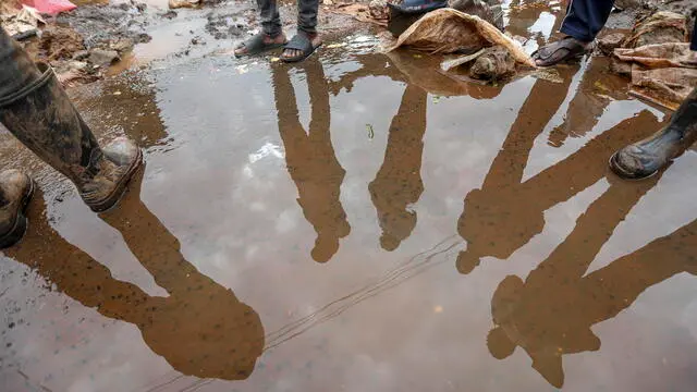 epa11304396 People are reflected on stagnant water as they gather around where a body of a man was discovered as the flooded Gitathuru River receeded three days after heavy rainfall broke its banks damaging the surrounding neighborhoods, in Mathare, Nairobi, Kenya, 27 April 2024. According to the Kenya Red Cross Society, the flooding left at least 75 dead as more bodies continue to be discovered, and more than 100,000 people have been affected by the March-May rains that continue to rise, including over 40,000 people displaced. Kenya's meteorological department predicts more heavy rainfall as floods continue to destroy properties in various parts of the country. EPA/Daniel Irungu