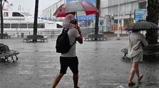 Cittadini e turisti genovesi tentano di ripararsi dalla pioggia. Allerta Gialla su tutta la Liguria per possibili temporali intensi. Genova, 30 giugno 2023. ANSA/LUCA ZENNARO
