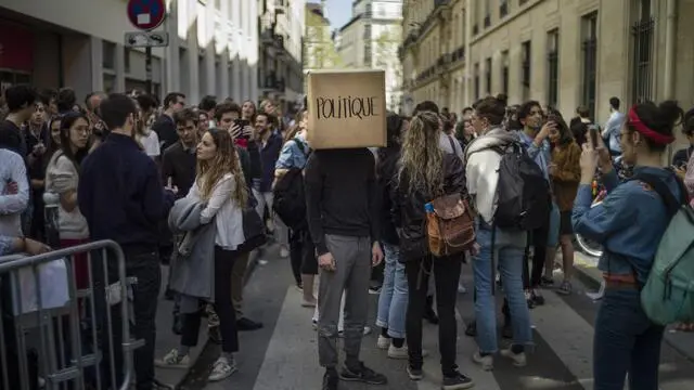epaselect epa06676955 A student of the 'Beaux Arts' (Art school) performs with a box on his head reading 'POLITICAL' as students of Sciences Po go on protest strike outside the Political Institute during a blockage in Paris, France, 18 April 2018. Several universities across France have been occupied to protest against the government's labor and education reforms. EPA/YOAN VALAT
