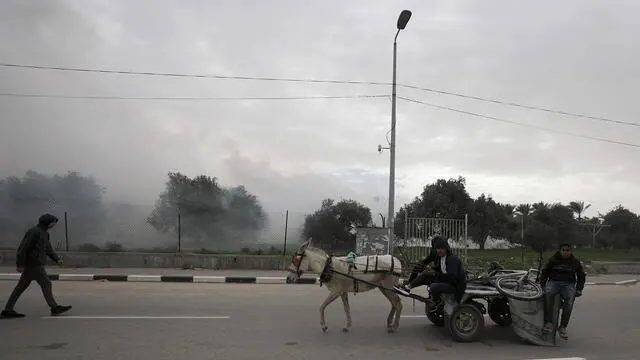 epa11041827 Palestinians on a donkey-drawn cart transit at a road as smoke rises after the Israeli army fired smoke bombs following an Israeli warning of increased military operations in the Al Nuseirat and Al Bureij refugee camps, Gaza Strip, 23 December 2023. More than 19,600 Palestinians and at least 1,300 Israelis have been killed, according to the Palestinian Health Ministry and the Israel Defense Forces (IDF), since Hamas militants launched an attack against Israel from the Gaza Strip on 07 October, and the Israeli operations in Gaza and the West Bank which followed it. The Israeli military stated that its forces are involved in 'ground operations' against Hamas across the Gaza Strip. EPA/MOHAMMED SABER