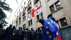 epa11338635 A protester waves a Georgian flag while wearing the European flag in front of policemen blocking a street during a rally against a draft bill on 'foreign agents' near the Parliament building in Tbilisi, Georgia, 14 May 2024. Georgian parliament deputies are set to adopt the law on 'foreign agents' at the plenary session on 14 May, in the third and final reading. Afterwards, the law will be sent to the Georgian president Salome Zourabichvili for signing, who has vowed to veto it. EPA/DAVID MDZINARISHVILI