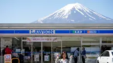 epa11330744 A foreign tourist poses in front of the Lawson Kawaguchiko Ekimae convenience store with Mount Fuji seen in the background, in Fujikawaguchiko, north of Mount Fuji, Japan, 10 May 2024. The town of Fujikawaguchiko in the northern foothills of Mount Fuji will block the view of Japan's iconic volcano with a curtain and metal bars from a particular spot in front of the Lawson convenience store that became popular in the last two years, in order to deter tourists who crowd the area to photograph it following complaints from locals. Town officials said there is a delay in the curtain preparation but the large fabric shall be installed in the second half of May. The Lawson convenience store franchise chain published an announcement to apologize for the inconvenience and concern caused to nearby residents and customers by the popularity of its stores as spots for photographing Mt Fuji. EPA/FRANCK ROBICHON