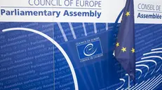 epa11434595 The logo of the Council of Europe pictured next to a European flag, in the Palace of Europe, during the third part of the 2024 Ordinary Session of the Parliamentary Assembly of the Council of Europe (PACE), in Strasbourg, France, 24 June 2024. The Parliamentary Assembly of the Council of Europe elects the new secretary general of the council of Europe to succeed Marija Pejcinovic Buric. EPA/ANTHONY ANEX