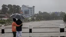 epa11462160 Two people take cover under an umbrella as they stand on a bridge overlooking the flooded Bagmati River after torrential rains in Kathmandu, Nepal, 06 July 2024. Nepal's National Disaster Risk Reduction and Management Authority (NDRRMA) warned of heavy monsoon rains that put several parts of the country at risk of floods and landslides. According to the statement issued by NDRRMA, at least 28 people have died in monsoon-related disasters since mid-June 2024. EPA/NARENDRA SHRESTHA