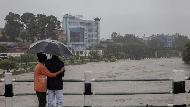 epa11462160 Two people take cover under an umbrella as they stand on a bridge overlooking the flooded Bagmati River after torrential rains in Kathmandu, Nepal, 06 July 2024. Nepal's National Disaster Risk Reduction and Management Authority (NDRRMA) warned of heavy monsoon rains that put several parts of the country at risk of floods and landslides. According to the statement issued by NDRRMA, at least 28 people have died in monsoon-related disasters since mid-June 2024. EPA/NARENDRA SHRESTHA