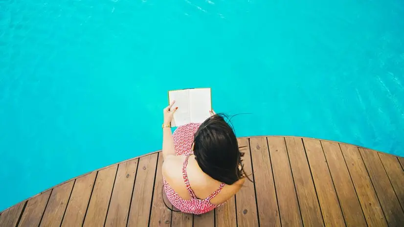 Una ragazza legge a bordo piscina