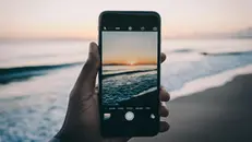Un uomo fa una foto al tramonto sul mare - Foto Unsplash