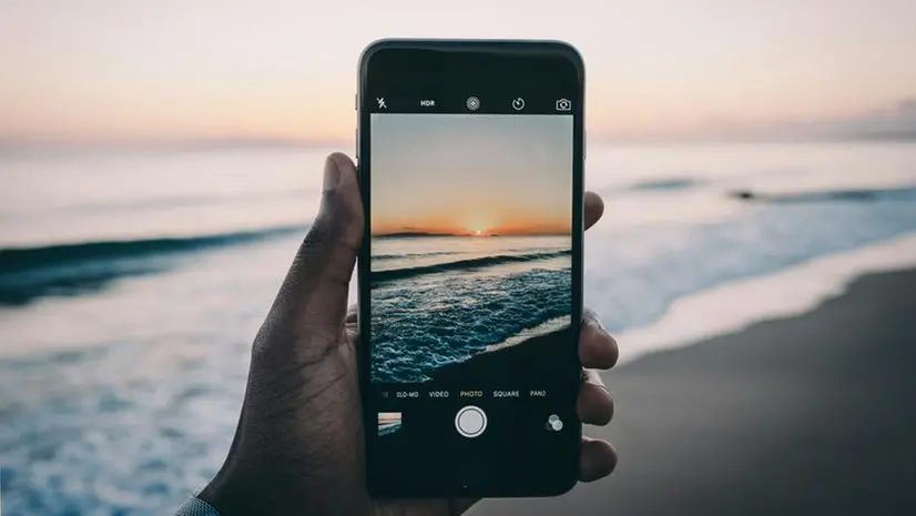 Un uomo fa una foto al tramonto sul mare - Foto Unsplash