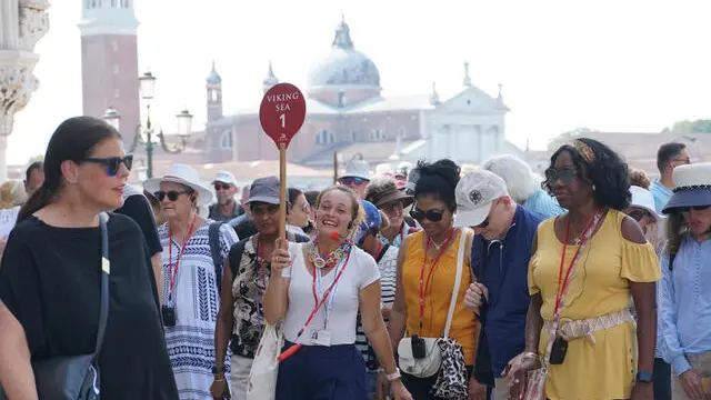 Una guida turistica accompagna un gruppo di visitatori verso piazza San Marco, usando un radio microfono per comunicare con loro, Venezia 1 agosto 2024: a partire da oggi l’amministrazione comunale applica l’ordinanza che impone la riduzione delle dimensioni delle comitive in visita nel centro storico e vieta l’uso di altoparlanti alle guide accompagnatrici. ANSA/ANDREA MEROLA