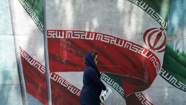 epa11547356 An Iranian woman walks past next to a wall painting of Iran's national flag on a street in Tehran, Iran, 13 August 2024. Tension remains high between Iran and Israel since late Hamas leader Ismail Haniyeh was killed in Tehran on 31 July 2024, as Iran's leader Ayatollah Khamenei had vowed for a 'harsh punishment' against Israel in retaliation over the killing of Haniyeh. US and EU administration asked Iran not to attack Israel. EPA/ABEDIN TAHERKENAREH