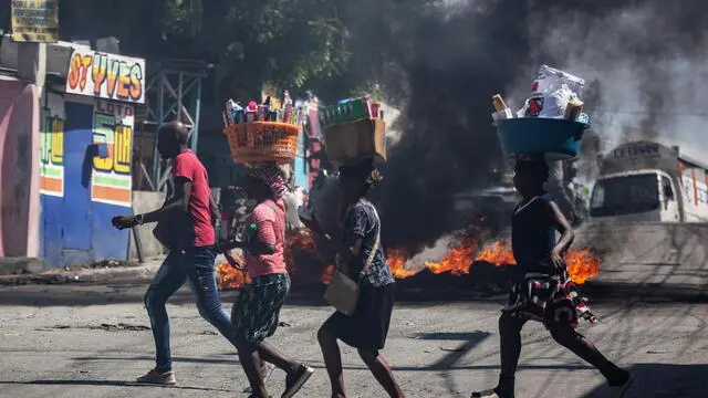 epa11555710 People carry their belongings as they move past a fire barricade during a protest against gang violence in the Solino neighborhood of Port-au-Prince, Haiti, 19 August 2024. EPA/MENTOR DAVID LORENS