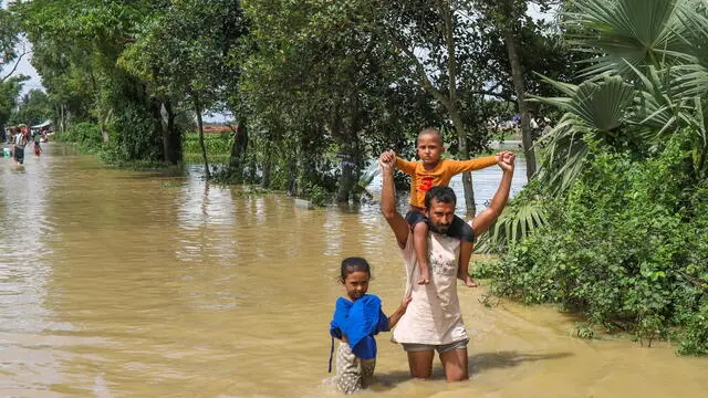 epa11565824 A man and his children ade through floodwater at a flood-affected area in Burichong, Comilla district, Bangladesh, 26 August 2024. According to the Disaster Management and Relief Ministry, at least 23 people have died and over five million have been affected by the floods triggered by heavy rain in Bangladesh. EPA/MONIRUL ALAM