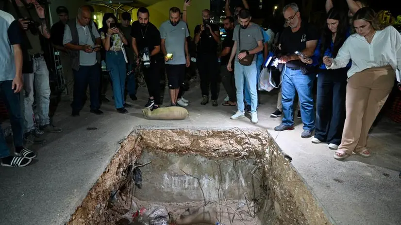 Persone in piedi vicino a un cratere dopo che i soldati dell'esercito libanese hanno fatto esplodere un dispositivo di comunicazione nel parcheggio dell'American University of Beirut Medical Center a Beirut