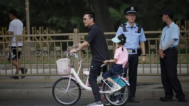 epa11479484 A man and a girl ride a bicycle next to a police officer near Tiananmen Square as China's communist party holds its third plenum in Beijing, China, 15 July 2024. The third plenum of the Chinese Communist Party's central committee will be held in Beijing for four days, from 15 to 18 July 2024. EPA/ANDRES MARTINEZ CASARES