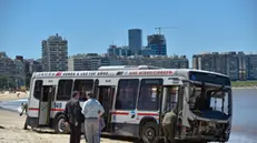 epa11685345 Officials inspect a bus that lost control and crossed the esplanade to end up on the shore of the beach in Montevideo, Uruguay, 26 October 2024. Sources from the Prosecutor's Office confirmed to EFE that, in addition, six people were slightly injured and three with minor injuries who were transferred to different health centers in the Uruguayan capital. EPA/Federico Gutierrez