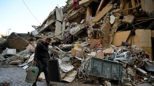 epaselect epa11672602 A man carries belongings as he walks past the site of an Israeli airstrike that targeted a branch of the Al-Qard Al-Hassan finance group in Al-Shiyah, Beirut, Lebanon, 21 October 2024. The Israeli military said the air forces conducted late on 20 October a series of targeted strikes against dozens of facilities and sites used by Al-Qard al-Hassan Association, an organization used by Hezbollah to finance its activities. The strikes were conducted in the areas of Beirut, southern Lebanon, and Baalbek. According to the Lebanese Ministry of Health, more than 2,460 people have been killed and over 11,500 others have been injured in Lebanon since the start of recent escalations of hostilities. EPA/WAEL HAMZEH