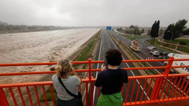 epa11691923 Two people stand on a bridge overlooking the Turia River, which is experiencing increased water levels after heavy rainfalls hit the city of Valencia, eastern Spain, 30 October 2024. The State Meteorological Agency (AEMET) has issued red alerts for rainfall in multiple regions of the province of Valencia, caused by the severe storm DANA. The storm has impacted multiple areas of the city, resulting in the loss of at least 13 lives due to flooding. EPA/BIEL ALINO
