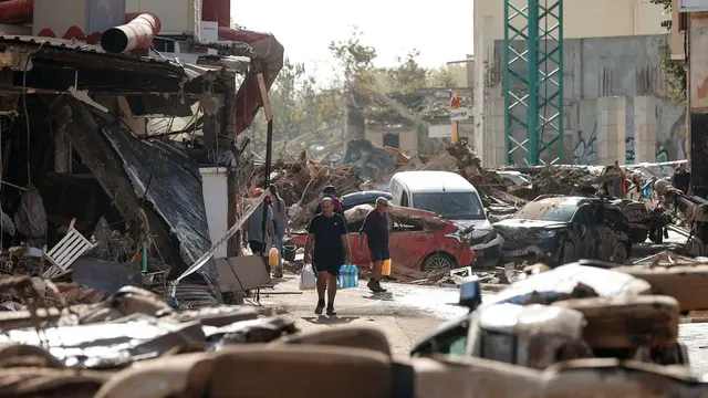 epa11693900 Residents carrying water bottles walk through a damaged street resulting from flooding in the Municipality of Catarroja, Valencia, Spain, 31 October 2024. At least 95 people died in the province of Valencia and neighboring provinces following floods caused by the DANA (high-altitude isolated depression) phenomenon impacting the eastern part of the country. EPA/MANUEL BRUQUE